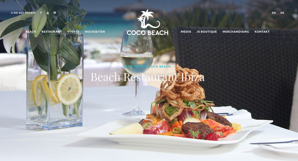 Screenshot der Coco Beach Webseite: Ein schön angerichteter Teller auf einem Tisch mit Weinglas im Hintergrund am Strand.