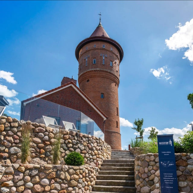Außeneingang des Wasserturms Bad Segeberg. Im Hintergrund der Wasserturm, davor Treppen bei blauem Himmel und Sonne.