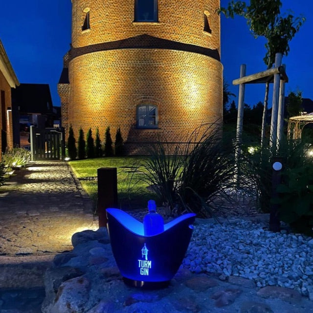Eine TURM GIN Flasche im LED-Eiswürfelbehälter vorm beleuchteten Wasserturm bei Nacht.