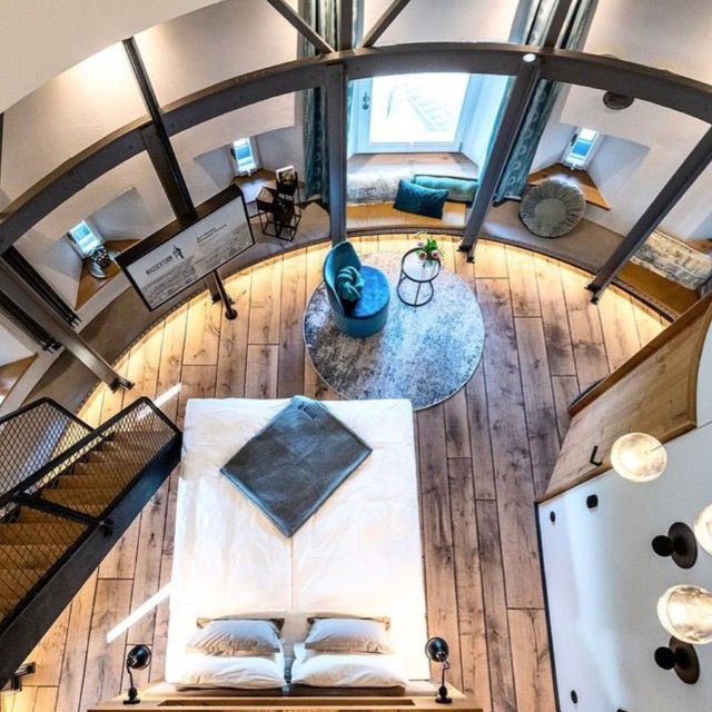 Rundes, stilvoll eingerichtetes Schlafzimmer mit Holzboden, Doppelbett und Fenstersitzbank von oben im Wasserturm Bad Segeberg.