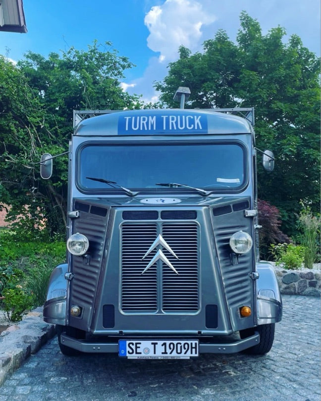 TURM GIN Truck von vorne auf einem Parkplatz mit Bäumen im Hintergrund.