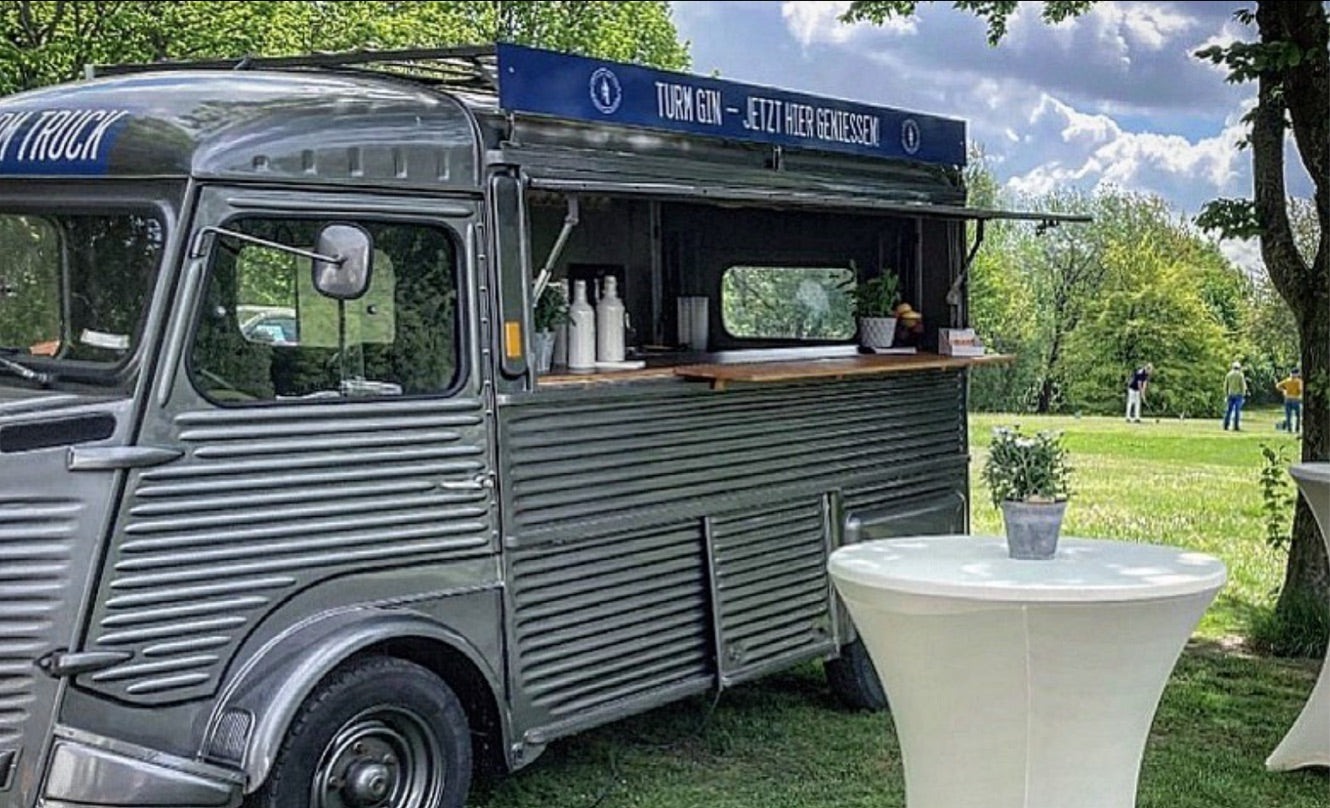 Geöffneter TURM GIN Truck auf einer grünen Wiese, davor Stehtische in Weiß.