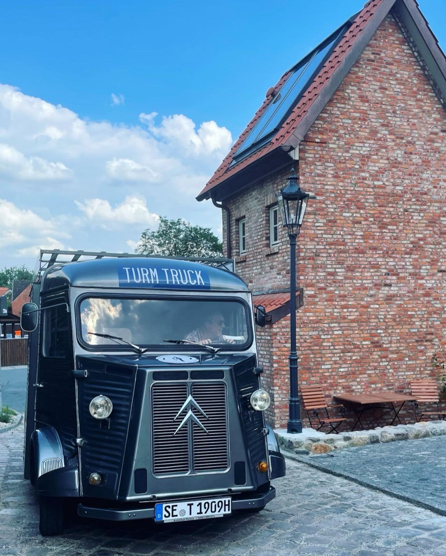 TURM GIN Truck auf einer Straße vor einem roten Backsteingebäude.