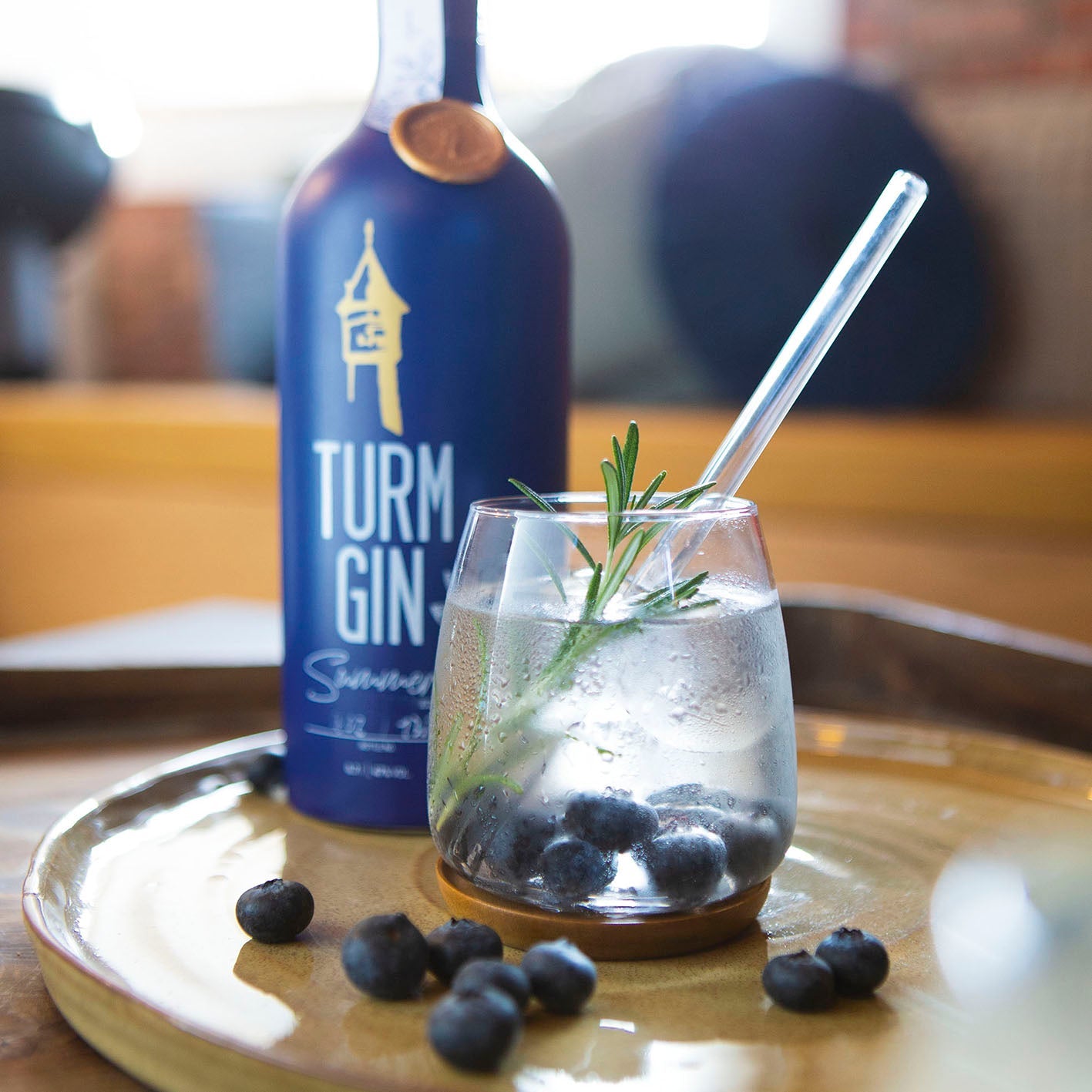 Gin mit Blaubeeren auf einem Tablett, dahinter die blaue Flasche der TURM GIN Summer Edition.
