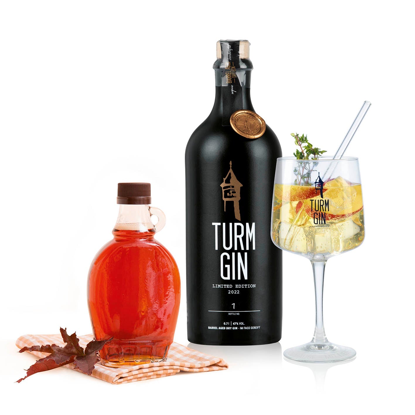 Schwarze Flasche des TURM GIN Barrel Aged - Limited Edition 20223 daneben Ahorn-Sirup in einer Flasche und ein fertiger Gin.