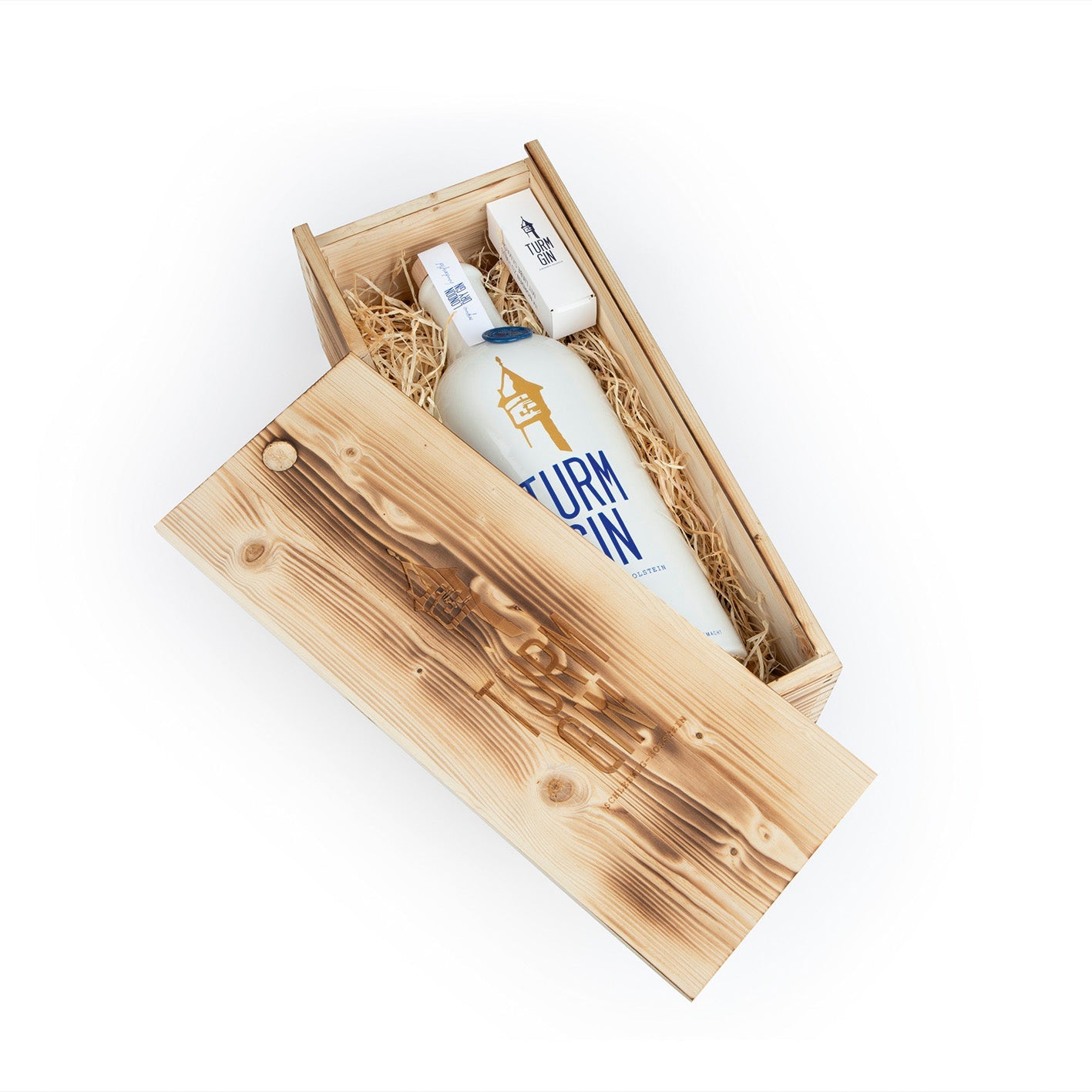 TURM GIN Magnum-Flasche mit 1,5 Litern verpackt in Holzverpackung auf Stroh daneben der Deckel vor weißem Hintergrund.