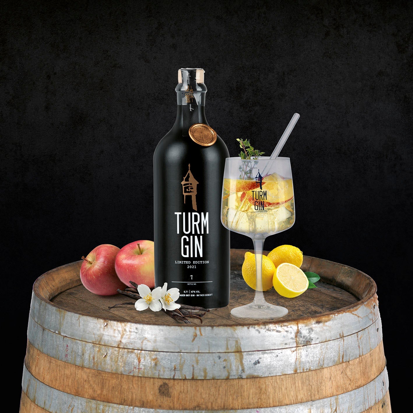 Schwarze TURM GIN Barrel Aged Flasche der Limited Edition 2021 mit Cocktail, Apfeln und Zitronen auf einem Holzfass.